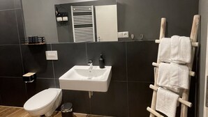 A modern bathroom with a toilet, sink, and towel rack. - Apartmenthaus Zeuthen 3 (Zeuthen)