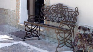 Un banc se trouve à l’extérieur d’un bâtiment doté d’un mur en pierre et d’une porte.