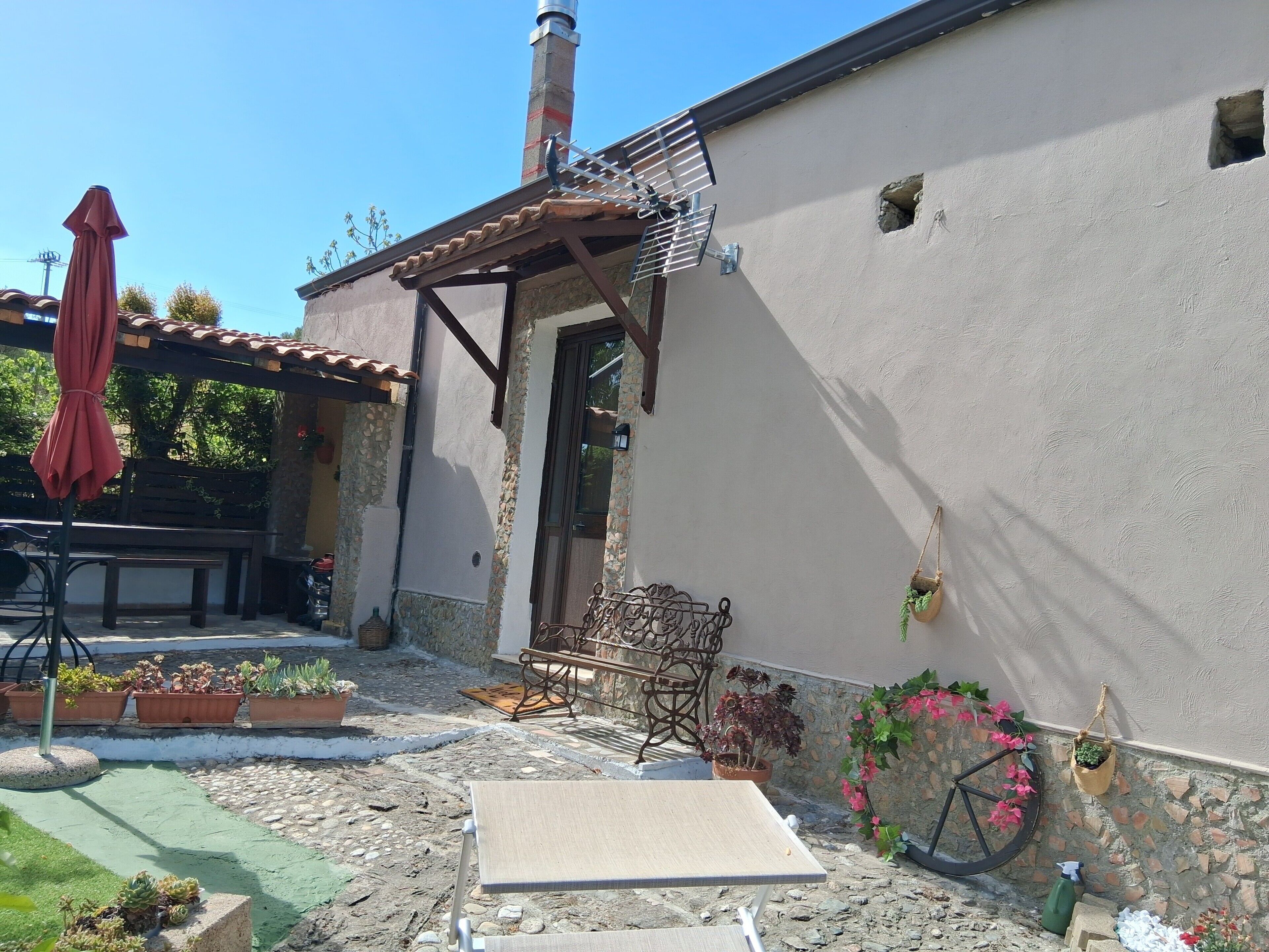 Une terrasse avec une table, des chaises, un parasol rouge, des plantes en pot et un vélo.