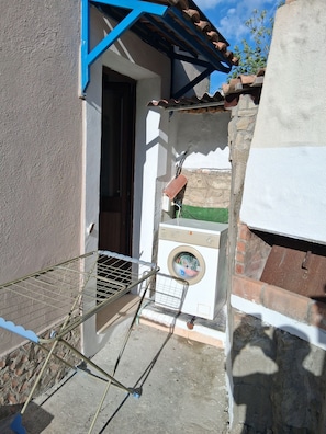 Un área de lavandería con lavadora, un tendedero de metal y una puerta que da a un espacio exterior cubierto.