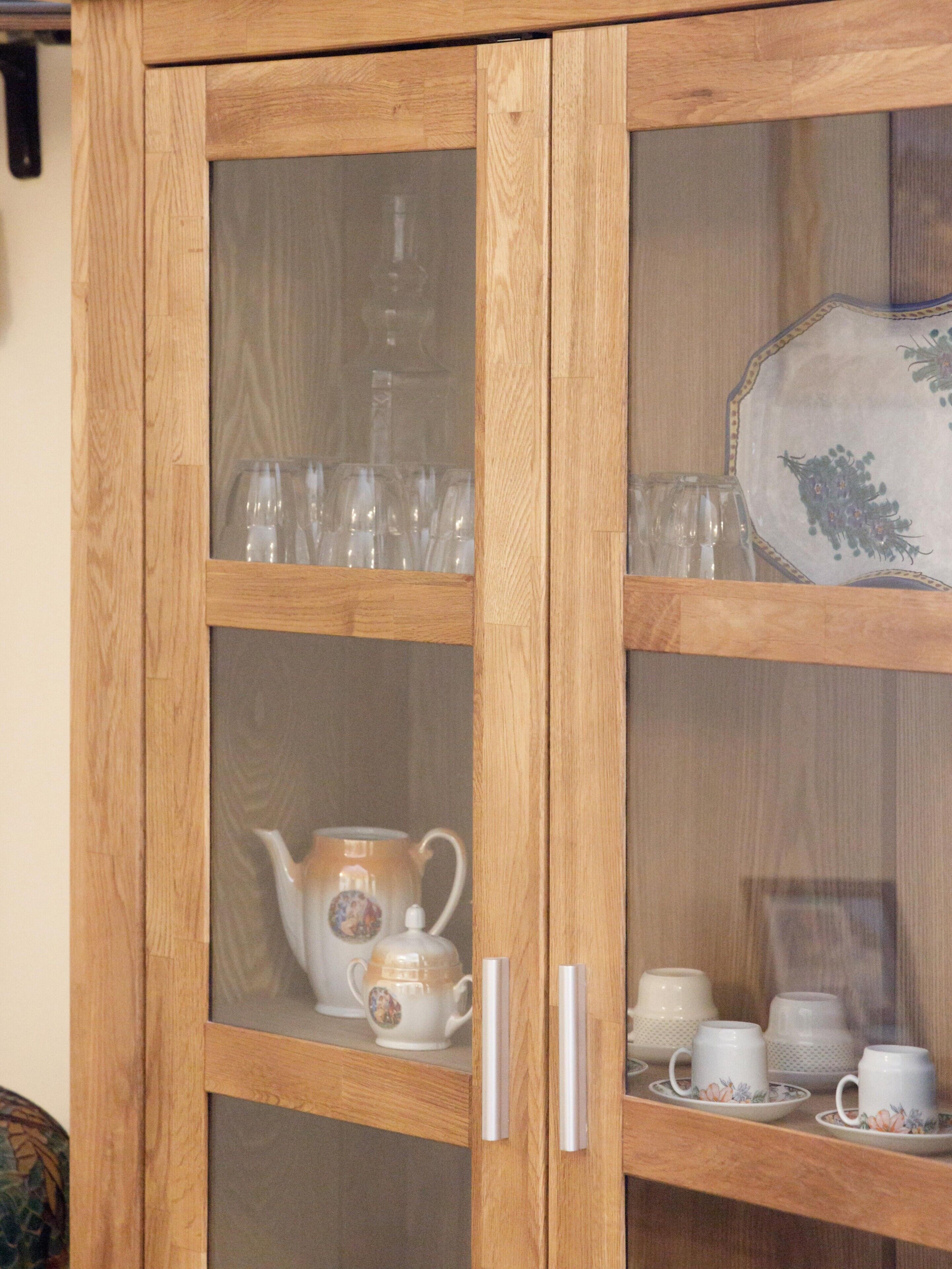 A wooden cabinet with glass doors containing tea sets and glassware.