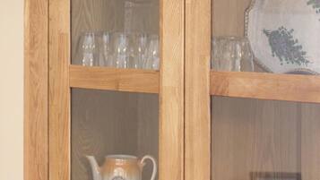 A wooden cabinet with glass doors containing tea sets and glassware.