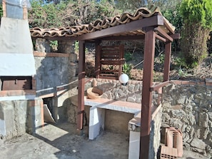 Una estructura de piedra con una pérgola de madera, una cesta tejida y macetas de terracota.