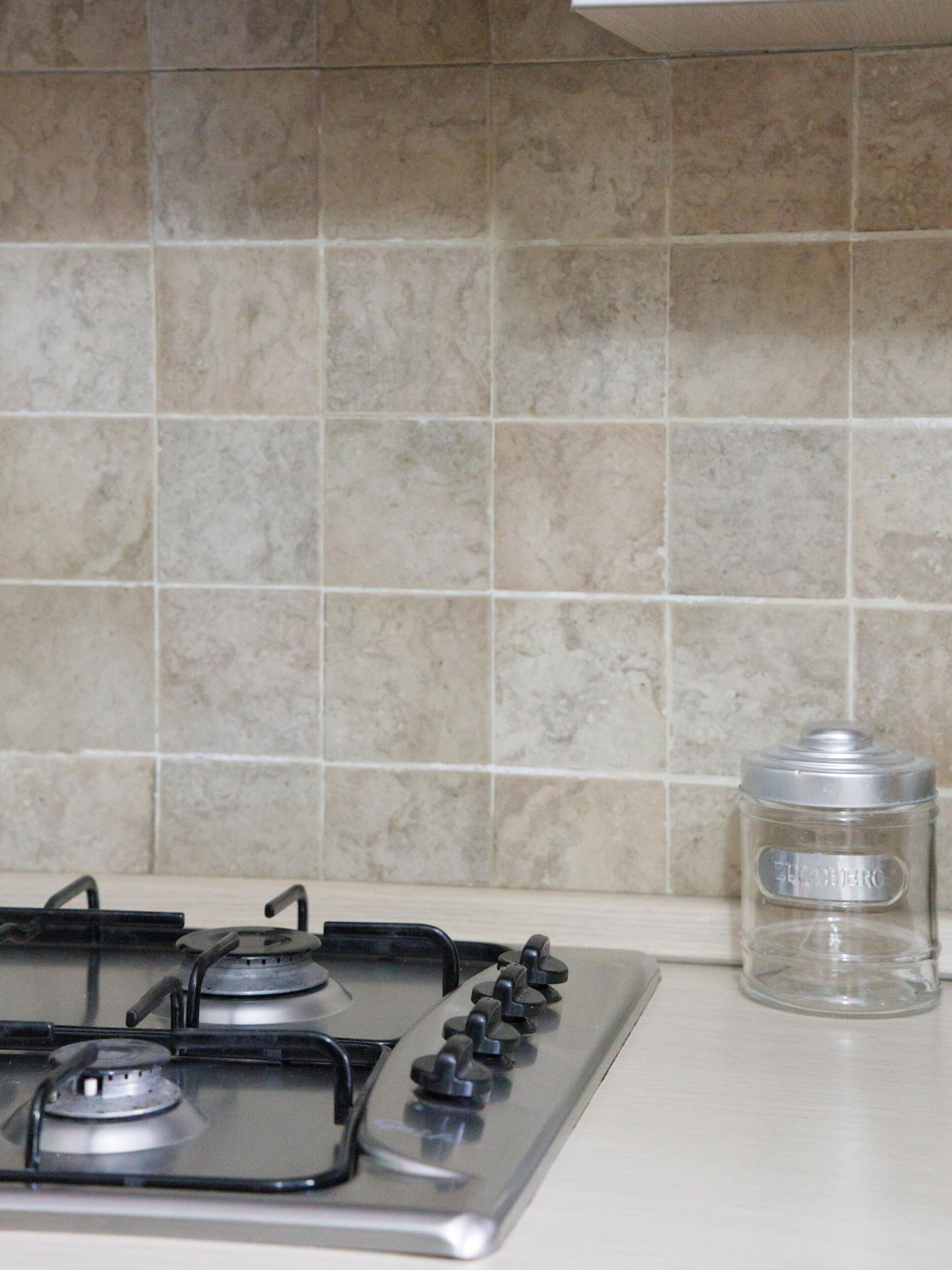 A kitchen with a gas stove, a clear glass container, and beige tiled walls.