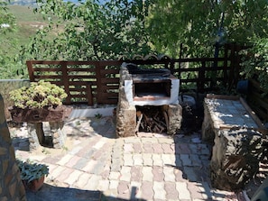 Un espacio de estar al aire libre rústico, con un horno de piedra, bancos de madera y plantas en macetas.