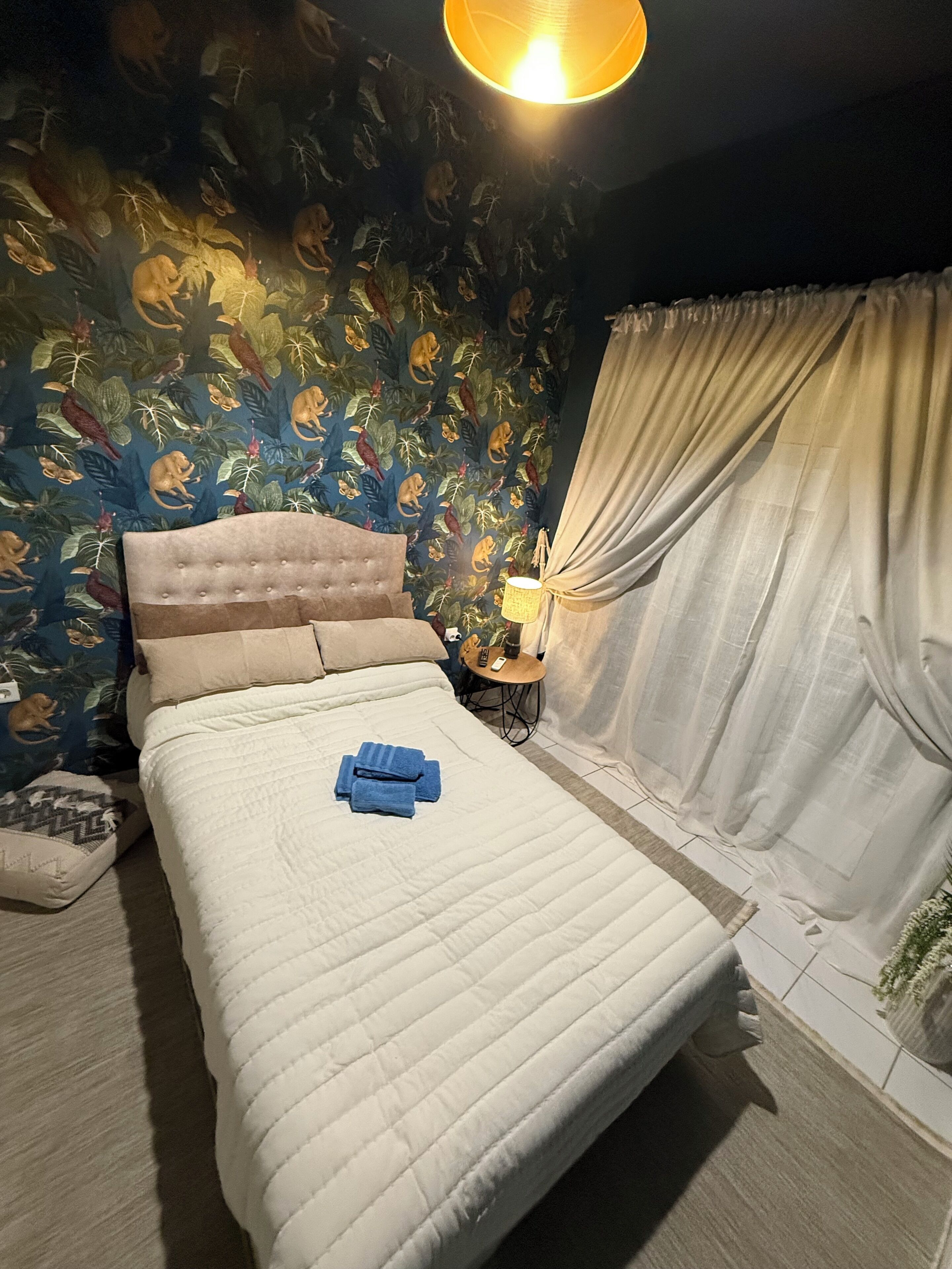 A bed with a quilt, a nightstand with a lamp, and a curtain.