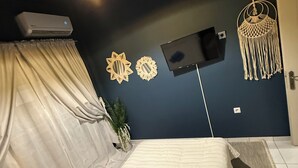 A bedroom with a bed, a TV, a wall-mounted air conditioner, and a macrame wall hanging. - RHODESIA guest house
Sea view apartment
Pet friendly
2’  beach (Chalkida)