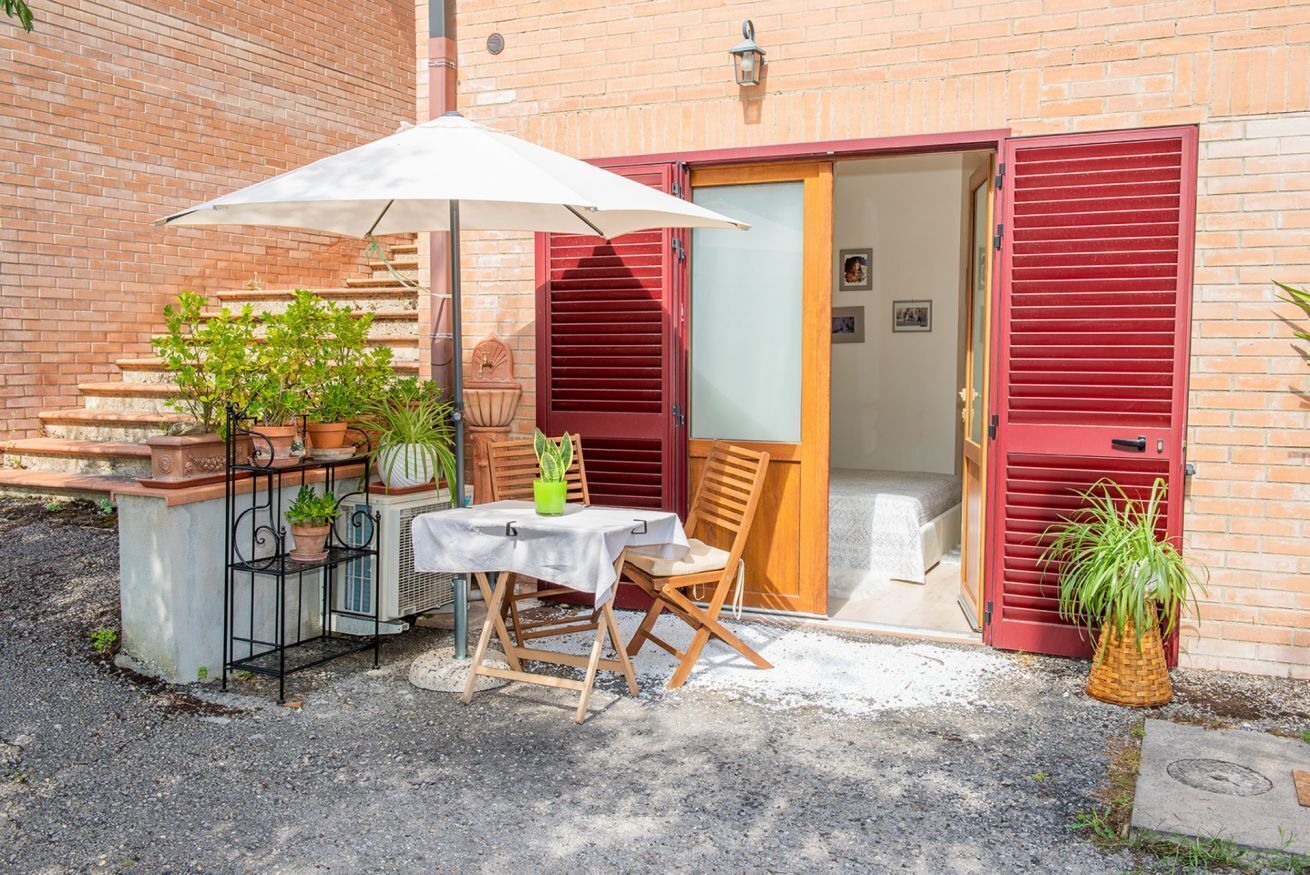 A patio with a table and chairs, potted plants, and a red door.