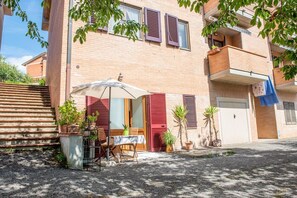 Ein Wohngebäude mit Balkon, Tisch mit Stühlen und Blumentöpfen.