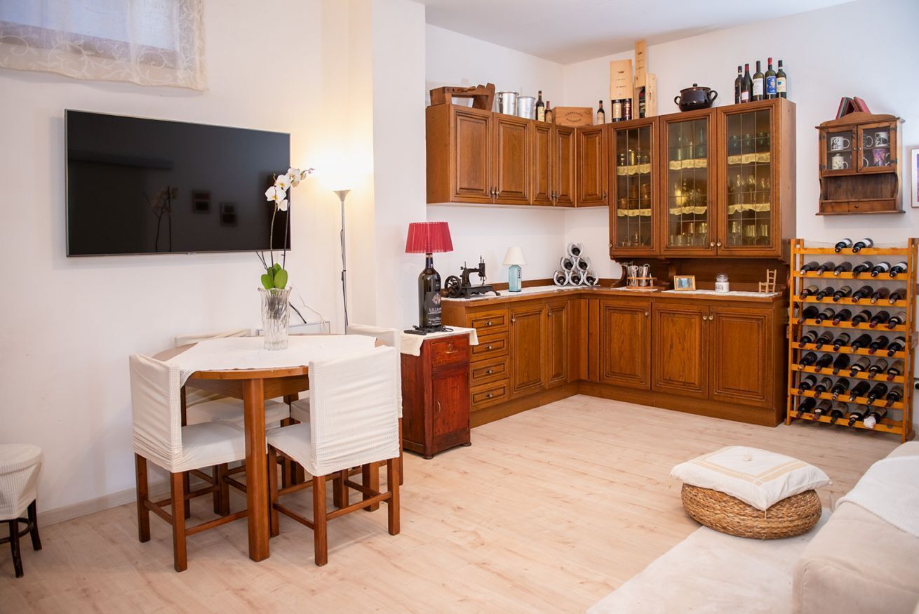 Eine moderne Küche mit Holzschränken, einem Essbereich mit Tisch und Stühlen, einem Weinregal und einem an der Wand befestigten Flachbildfernseher.