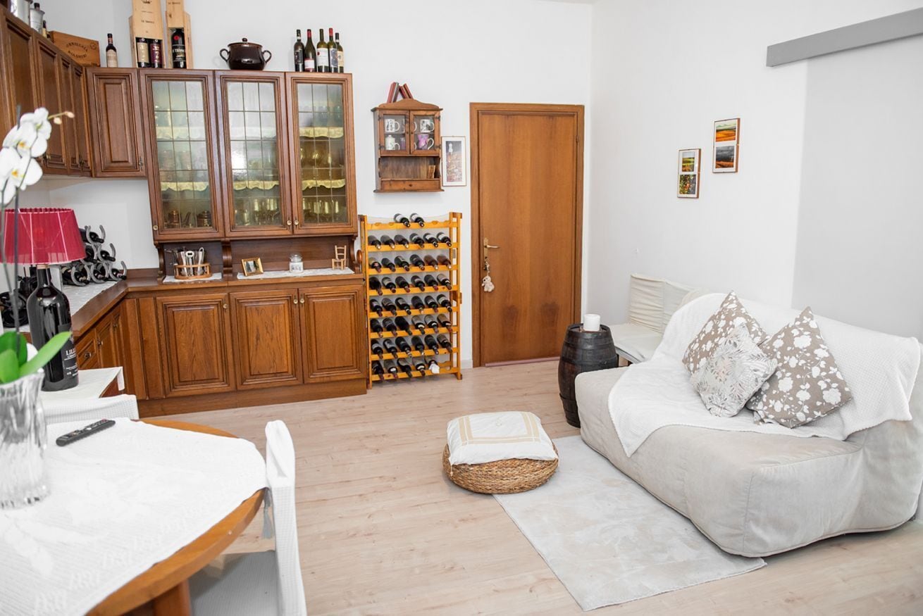 Una sala de estar con sofá, una mesa de comedor y una zona de cocina con armarios y una vinoteca.
