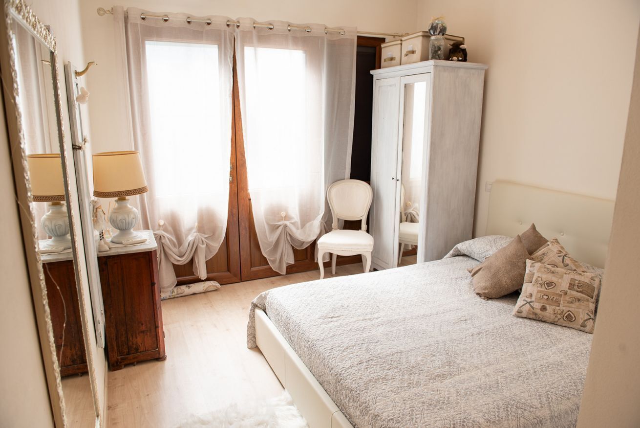 A bedroom with a bed, a chair, a wardrobe, and a mirror.
