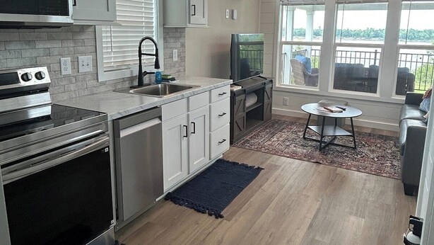 A modern kitchen with built-in appliances, a dining area with a table and chairs, and a balcony with outdoor seating. - Harbor Light | Modern Tiny Home with River Charm (Vicksburg)