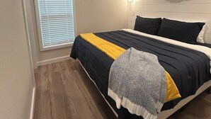 A bedroom with a bed, a window with blinds, an air conditioning unit, and a wooden floor. - Harbor Light | Modern Tiny Home with River Charm (Vicksburg)