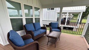 A covered outdoor seating area with wicker furniture and a wooden deck. - Harbor Light | Modern Tiny Home with River Charm (Vicksburg)