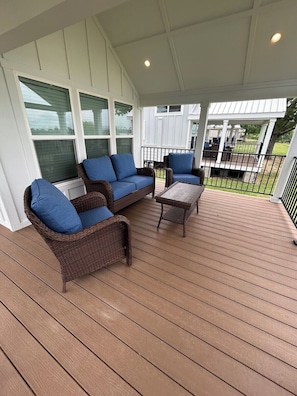 A covered outdoor seating area with wicker furniture and a wooden deck. - Harbor Light | Modern Tiny Home with River Charm (Vicksburg)