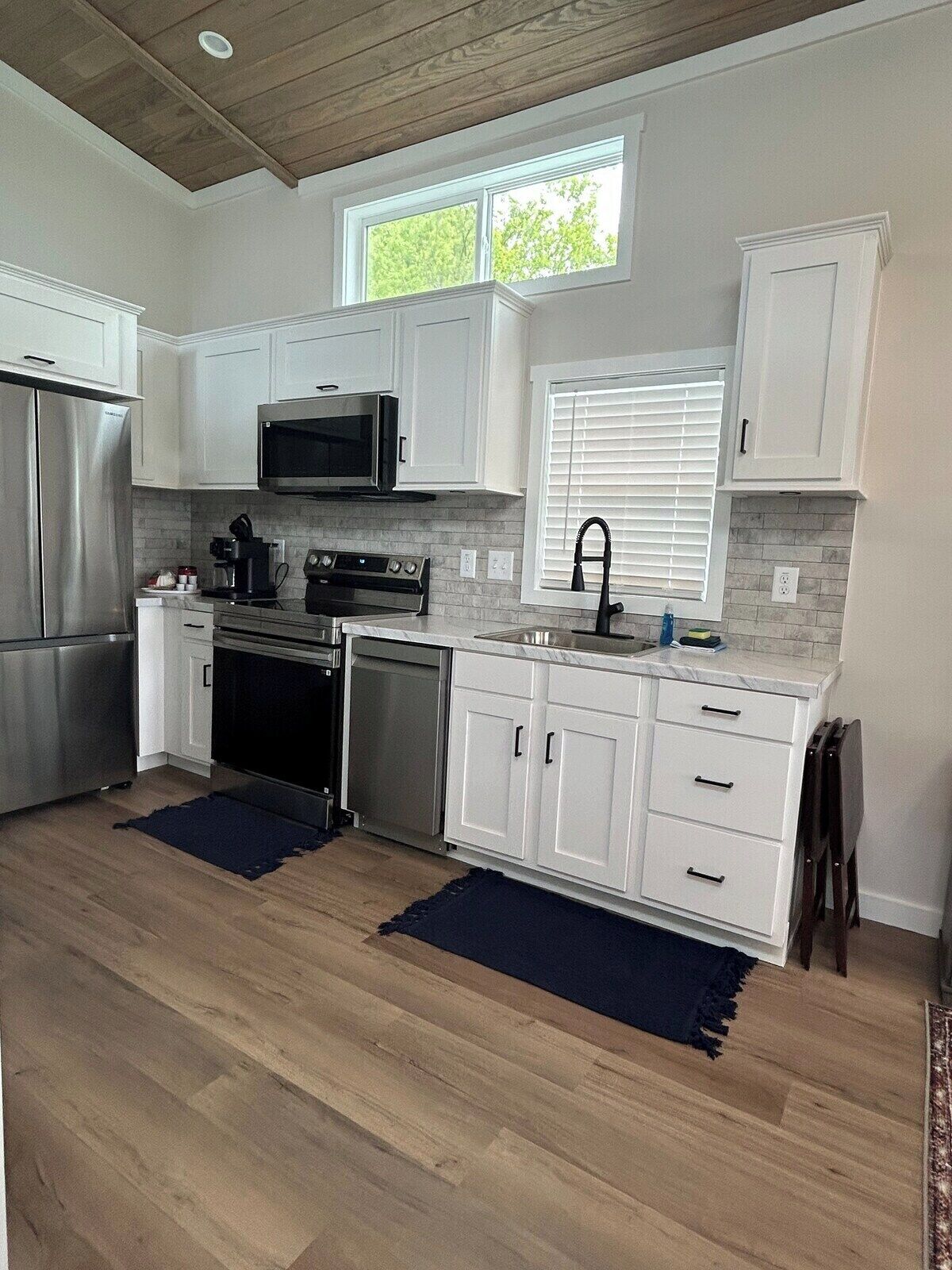 A modern kitchen with white cabinetry, stainless steel appliances, and a window with blinds.