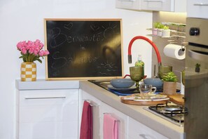 Una cocina con una pizarra mostrando un mensaje, un jarrón de flores rosadas y diversos utensilios de cocina.
