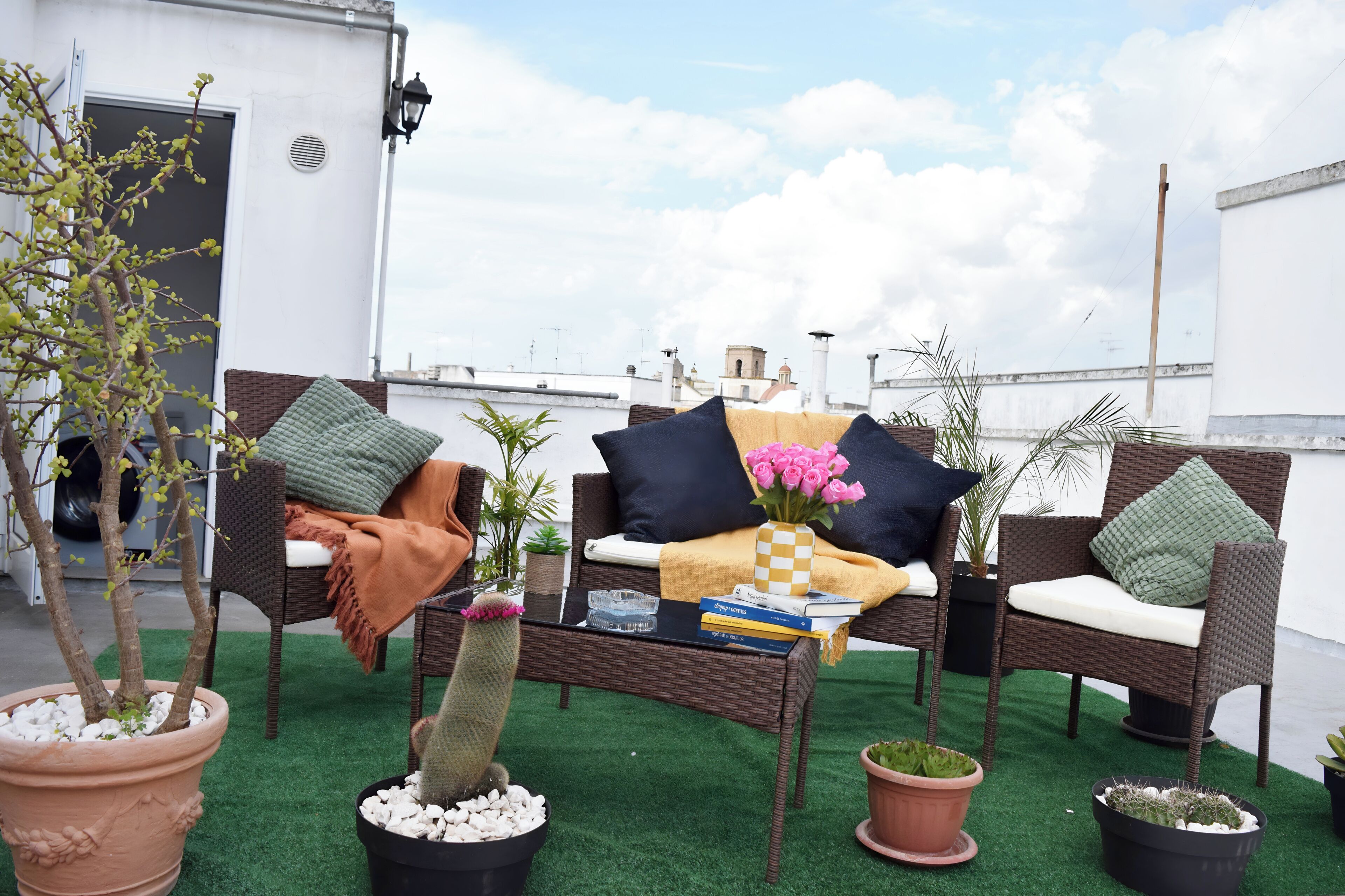 Una terraza en la azotea con mobiliario de mimbre, un cactus y diversas plantas en macetas.