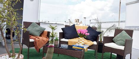 A rooftop terrace with wicker furniture, a cactus, and a variety of potted plants.