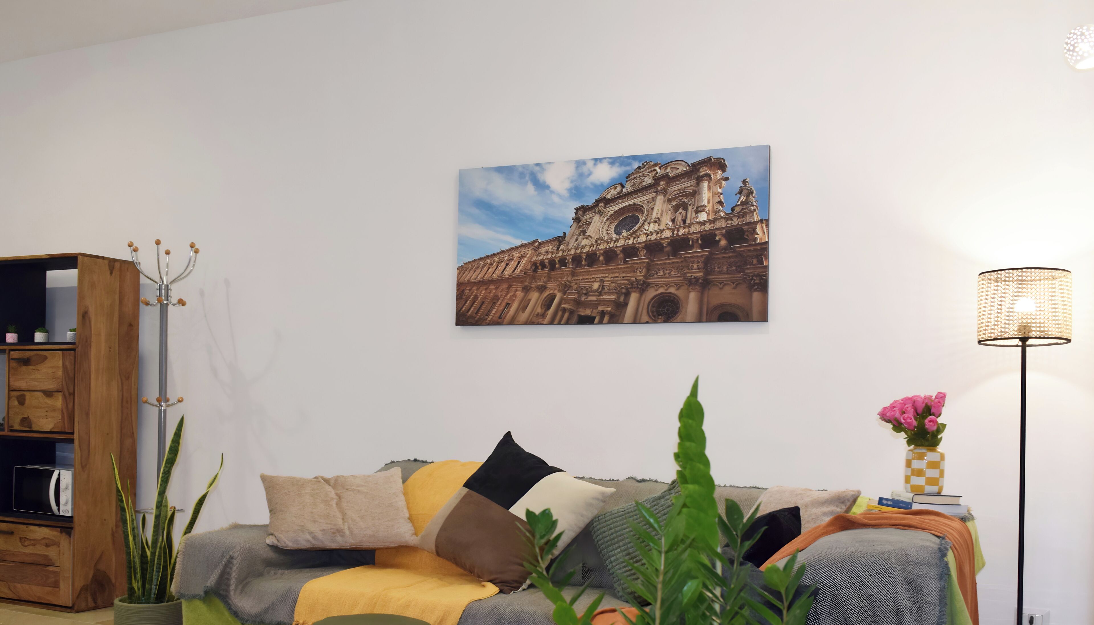 A living room with a sofa, a wooden cabinet, a floor lamp, and a painting of a historical building.