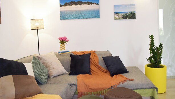 Una sala de estar con sofá, almohadas, lámpara y cuadros en la pared.