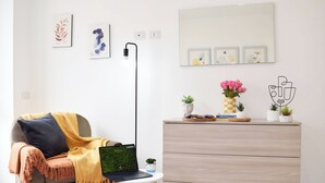 Una sala de estar moderna con un sofá, una mesita con una computadora portátil, una lámpara de pie y un aparador con objetos decorativos.
