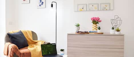 Ein modernes Wohnzimmer mit einer Couch, einem kleinen Tisch mit einem Laptop, einer Stehlampe und einer Kommode mit dekorativen Accessoires.