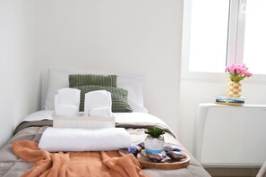A neatly made bed with pillows, a tray with snacks, and a vase with flowers on a bedside table.