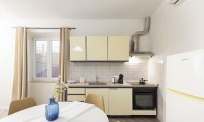 Una cocina compacta con comedor, una ventana con cortinas, horno empotrado y cafetera.