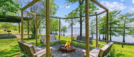 A wooden gazebo with a fire pit in the center, surrounded by benches.