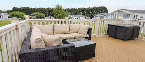 A deck with a wicker sofa and a table, surrounded by a white fence.