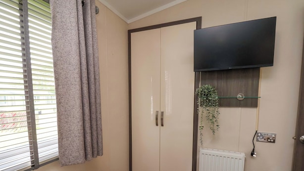 A bedroom with a bed, a wardrobe, a radiator, a TV, and a window with blinds. - Finch 66 (Scarborough)