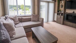 A modern living room with a sectional sofa, a coffee table, a flat-screen TV, and a sliding glass door leading to a balcony. - Finch 66 (Scarborough)