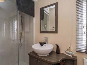 A bathroom with a glass shower enclosure, a white sink, a mirror, and a window with blinds. - Finch 66 (Scarborough)