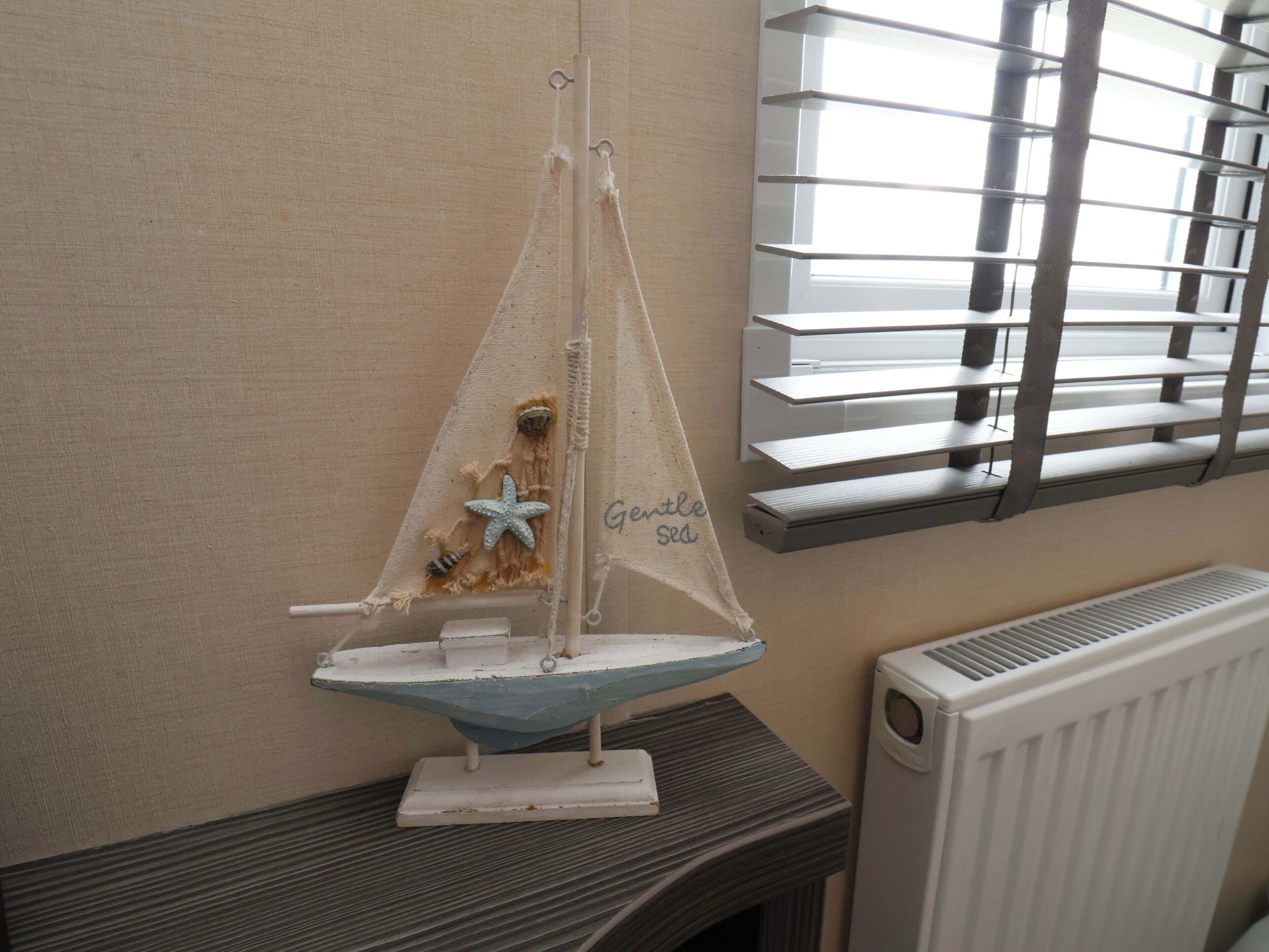 Ein Modellsegelboot auf einem Regal, ein Fenster mit Jalousien und eine Heizung.