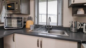 A kitchen with a microwave, toaster, sink, and a window with blinds. - Finch 66 (Scarborough)