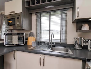 A kitchen with a microwave, toaster, sink, and a window with blinds. - Finch 66 (Scarborough)