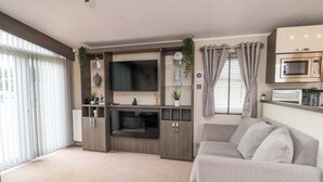A living room with a flat-screen TV, a fireplace, a sofa, and a kitchenette with a microwave. - Finch 66 (Scarborough)