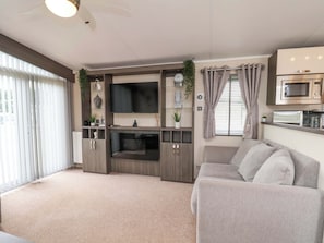 A living room with a flat-screen TV, a fireplace, a sofa, and a kitchenette with a microwave. - Finch 66 (Scarborough)