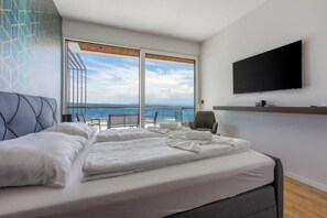 A hotel room with a bed, a TV, a chair, and a balcony with a view of the ocean. - Villa Carolea (Crikvenica)