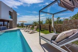 A modern pool area with lounge chairs, a glass enclosure, and a stone wall. - Villa Carolea (Crikvenica)