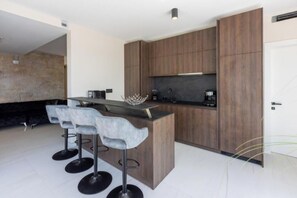 A modern kitchen with a central island, bar stools, and wooden cabinets. - Villa Carolea (Crikvenica)
