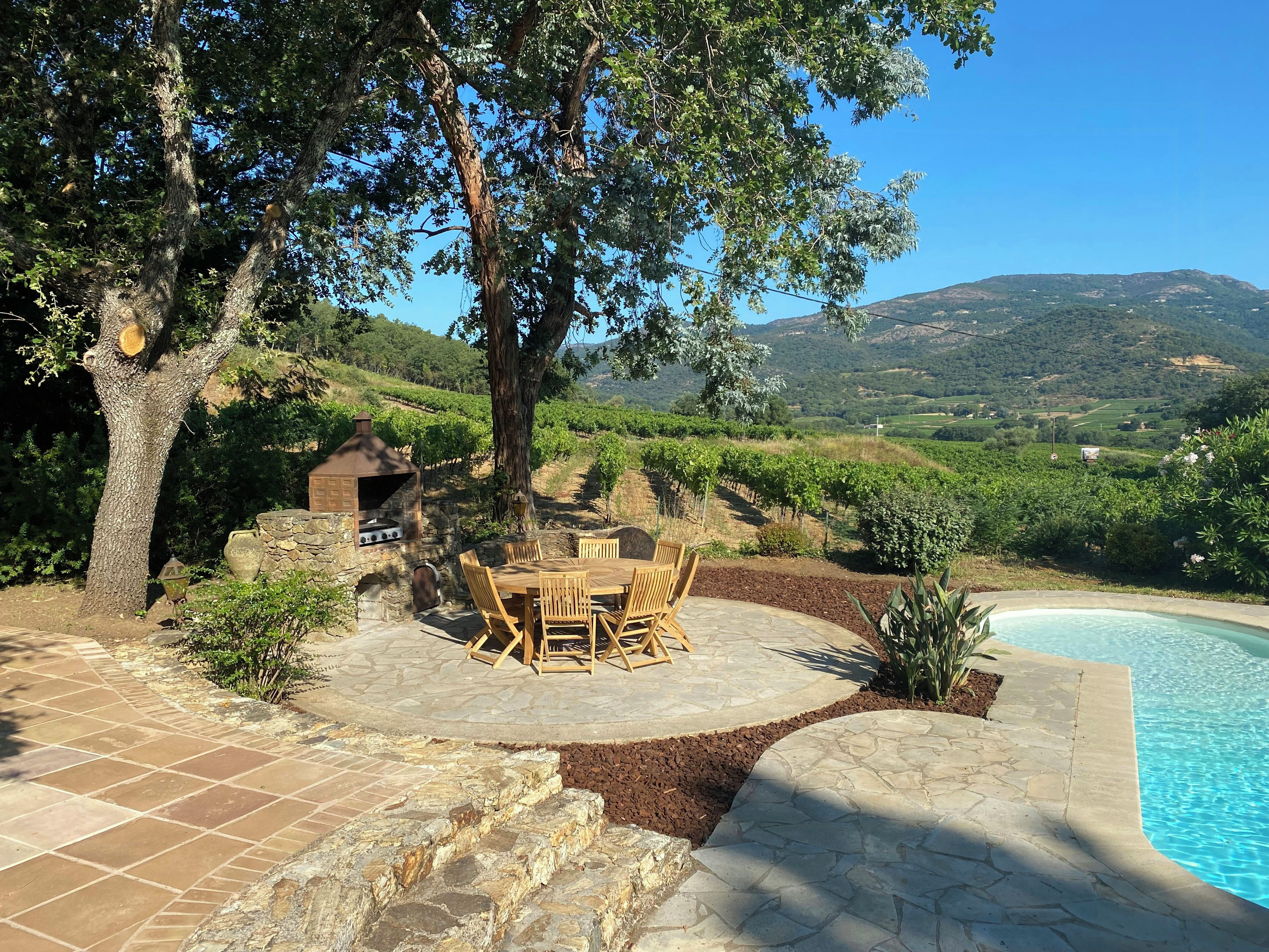 A patio with a stone table and chairs, a barbecue grill, and a pool.