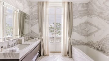 A bathroom with a marble floor, a bathtub, a sink with a mirror, and a view through a glass door.