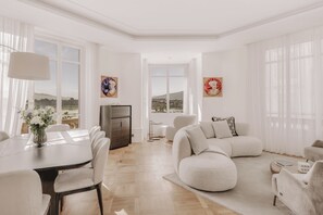 A spacious living room with a dining area, large windows, and artwork on the walls. - Ultima Quai Wilson Geneva (Genève)