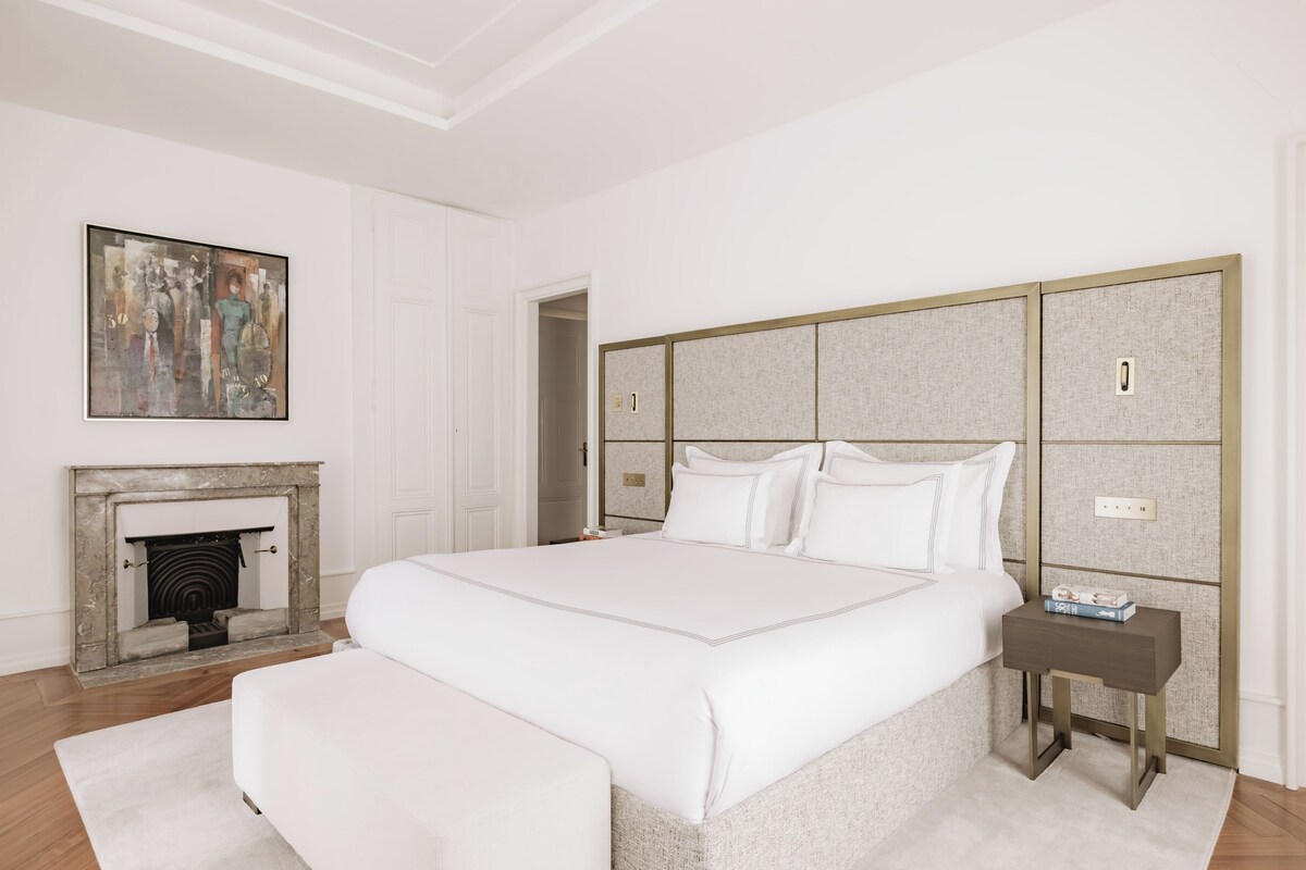 A modern bedroom with a large bed, a fireplace, and a painting on the wall.