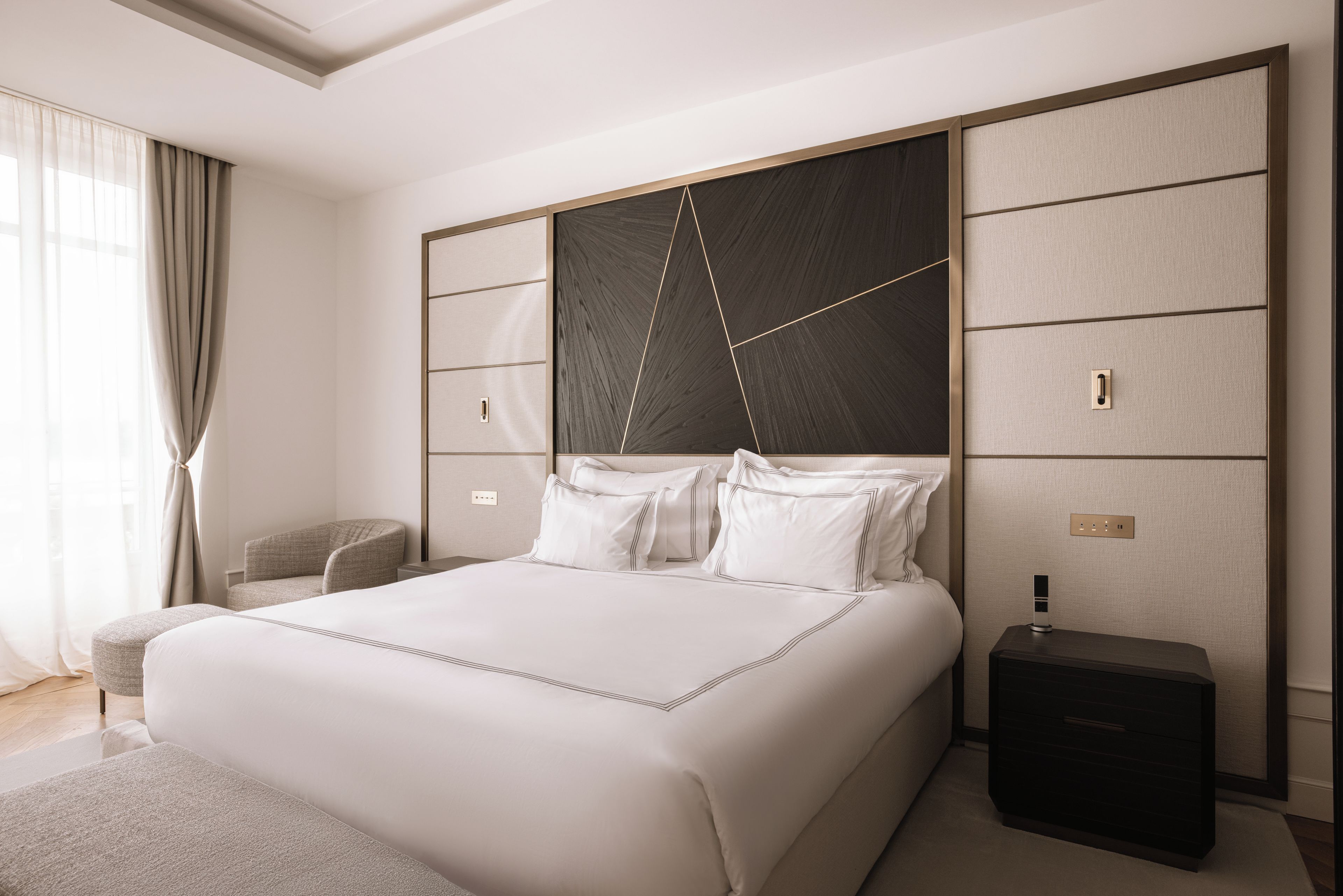 A modern hotel room with a large bed, a bedside table, a nightstand, and a window with curtains.