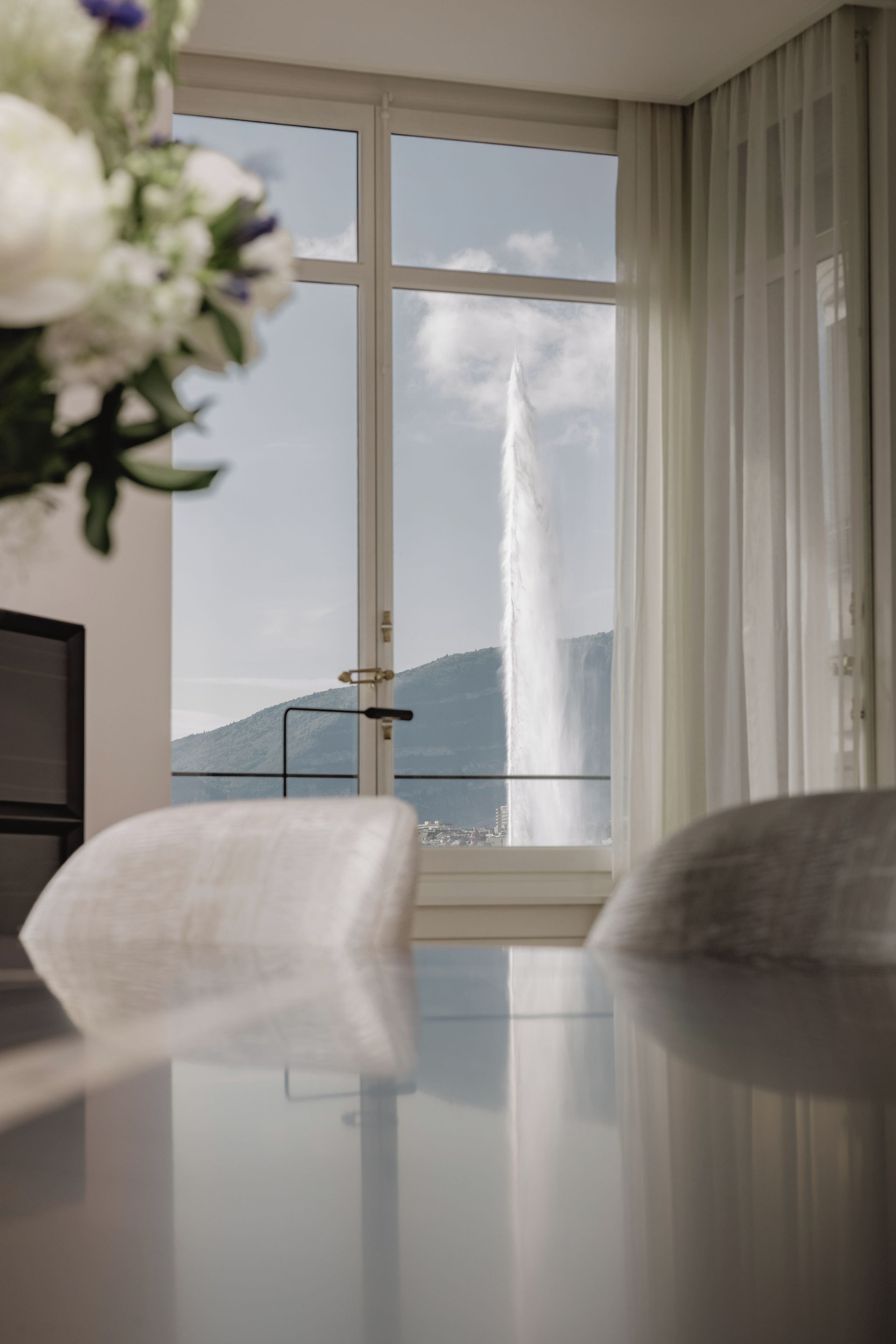 Een kamer met uitzicht op een waterval door een groot raam, een flatscreen televisie en een bloevas op een tafel.