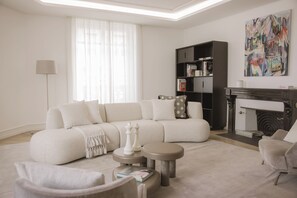 A modern living room with a sectional sofa, a fireplace, a bookshelf, and a large abstract painting. - Ultima Quai Wilson Geneva (Genève)